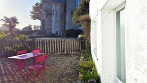 Un edificio de piedra con fachada blanca, una valla de madera y una mesa y sillas rojas al frente.