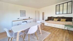 A modern living room with a dining area, a sofa, and a large window. - Le nid de port-lin - Les Gîtes de la Côte d'Amour (LE CROISIC)