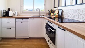A compact kitchen with a dishwasher, oven, and a window with a view. - Le nid de port-lin - Les Gîtes de la Côte d'Amour (LE CROISIC)
