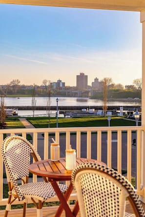 A balcony with two wicker chairs and a small table, overlooking a river with buildings in the background. - Harborside | Golf | Pool | Marina Views (St Joseph)