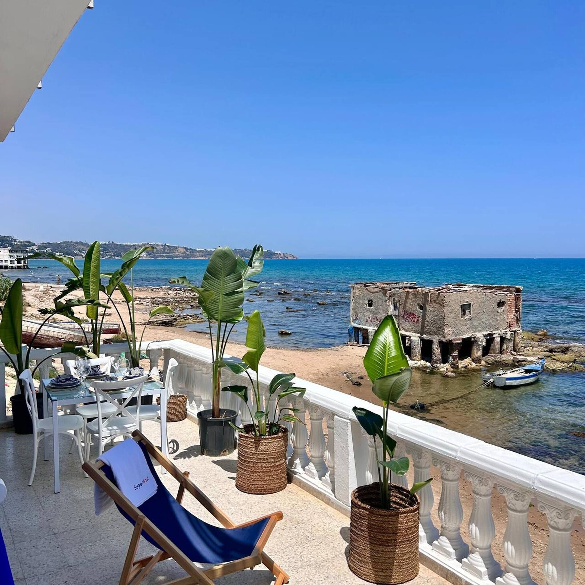 Un balcon avec vue sur la mer, une chaise et des plantes en pot.