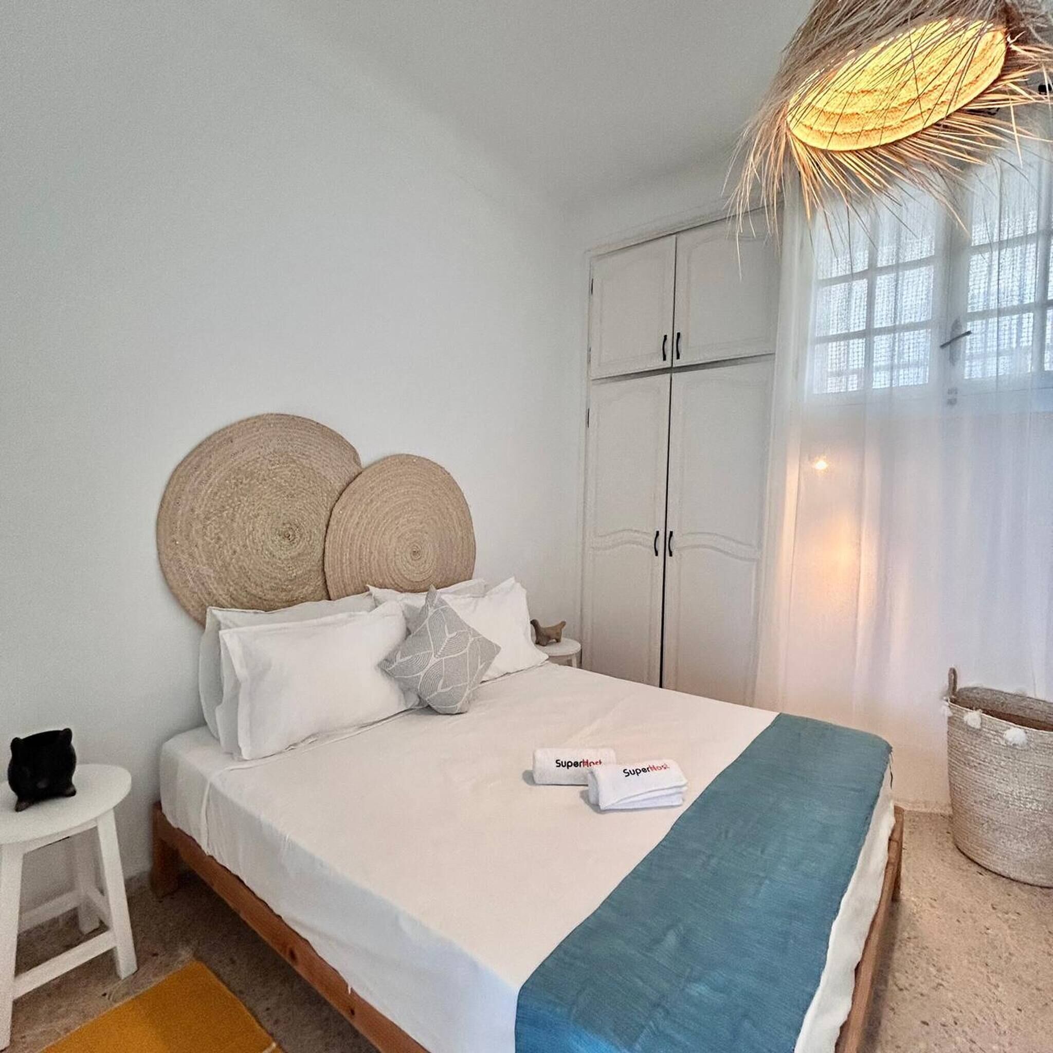 Uma cama com colchão branco, duas cabeceiras redondas trançadas e um cobertor azul.
