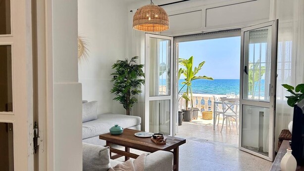 A room with a sofa, a table, and a view of the sea through large glass doors. - Maison Azur à la Marsa Plage (La Marsa)