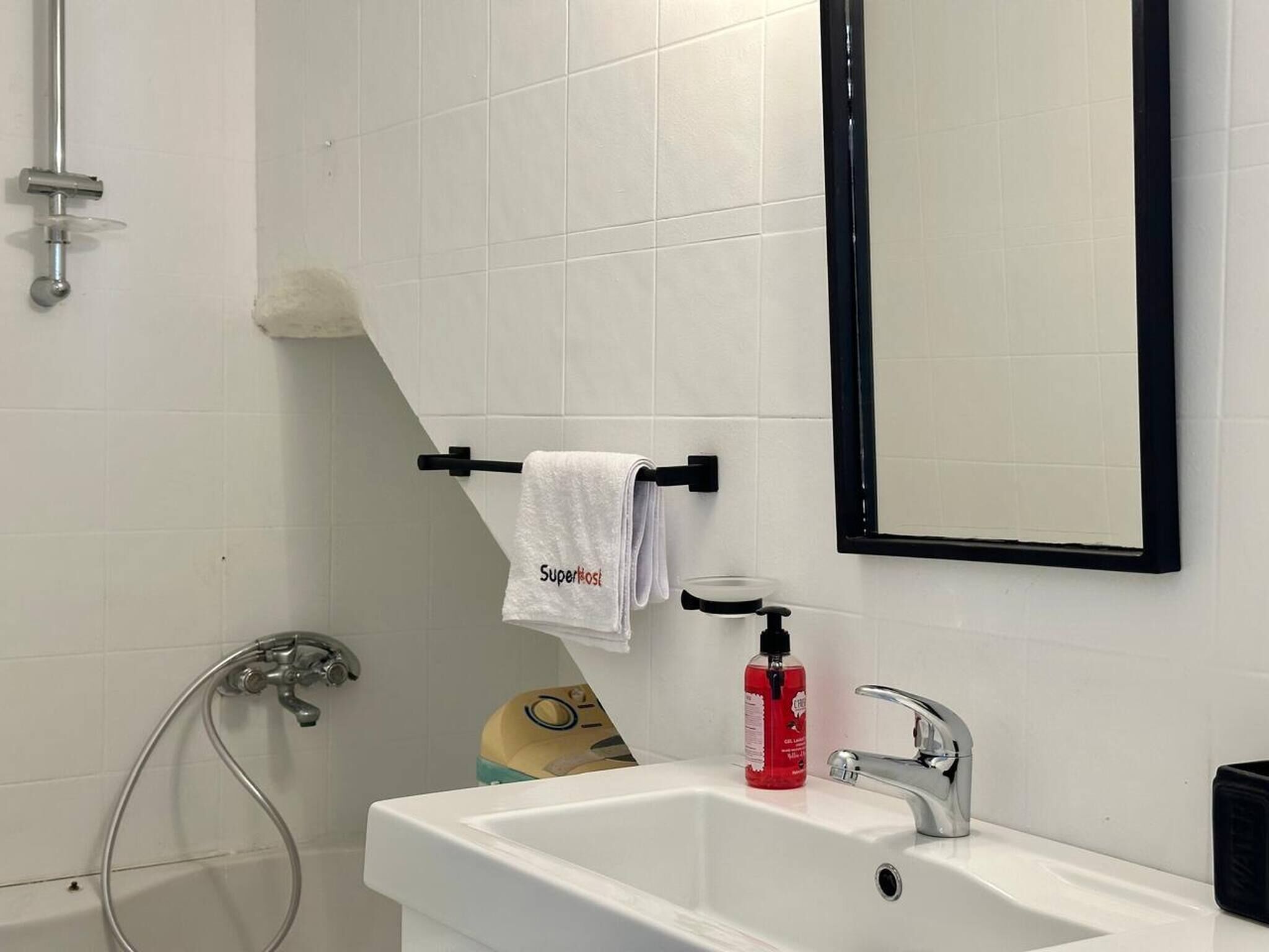 A bathroom with a white sink, a handheld showerhead, a towel rack with a towel, and a bottle of red liquid.