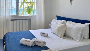 A bedroom with a bed, a window with curtains, a view of the sea, and a tropical plant outside. - Maison Azur à la Marsa Plage (La Marsa)