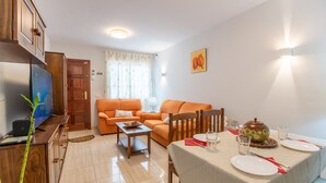 Una sala de estar con sofá, una mesa de comedor con platos y vasos, un televisor y un mueble.