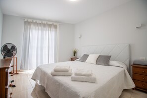 Een keurig opgemaakt slaapkamer met een bed, nachtkastjes, een ventilator en een raam met gordijnen.