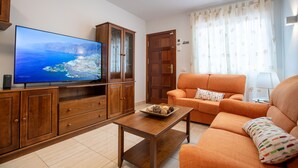 Una sala de estar con televisor, armarios de madera, un sofá naranja y una mesa de centro.
