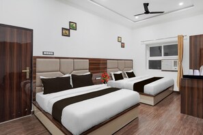 A hotel room with two beds, a wooden headboard, a ceiling fan, and a window with curtains. - Super Collection Varanasi Suites (Varanasi)