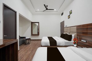 A hotel room with two beds, a desk, a chair, a small table with a kettle, a mirror, and a ceiling fan. - Super Collection Varanasi Suites (Varanasi)