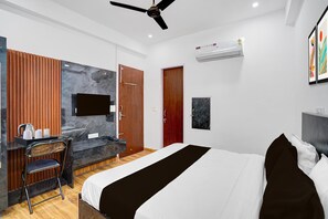 A modern hotel room with a bed, a desk with a chair, a ceiling fan, and an air conditioning unit. - Townhouse Khandsa Road Gurugram (Gurugram)