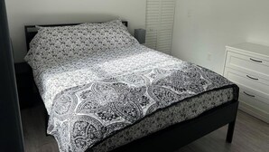 A bed with a patterned bedspread, a bedside table, a wardrobe, and a wall with a framed picture. - Trendy Bungalow near Armature and Downtown Tampa (Tampa)