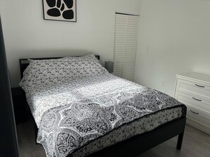 A bed with a patterned bedspread, a bedside table, a wardrobe, and a wall with a framed picture. - Trendy Bungalow near Armature and Downtown Tampa (Tampa)