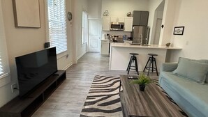 A modern living room with a flat-screen TV, a sofa, a coffee table, and a kitchen in the background. - Trendy Bungalow near Armature and Downtown Tampa (Tampa)
