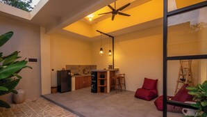 Ein offener Wohnbereich mit Küche, Deckenventilator, Pendelleuchten und einem roten Sessel.