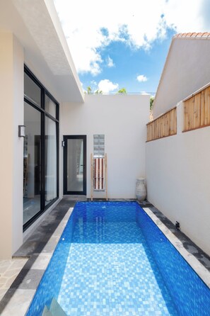 A modern swimming pool with a tiled floor, a glass door entrance, and a wooden fence. - Rinta Villas (Pecatu)