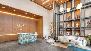 A reception area with a wooden wall, a reception desk, a seating area with a sofa and chairs, and a shelving unit with decorative items. - Modern Downtown Miami Studio - Rooftop Pool (Miami)
