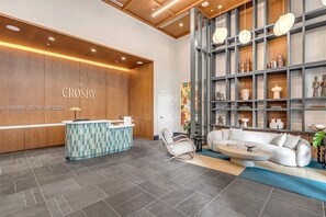 A reception area with a wooden wall, a reception desk, a seating area with a sofa and chairs, and a shelving unit with decorative items. - Modern Downtown Miami Studio - Rooftop Pool (Miami)