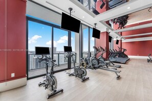 A modern gym with cardio machines, large windows, and a city view. - Modern Downtown Miami Studio - Rooftop Pool (Miami)