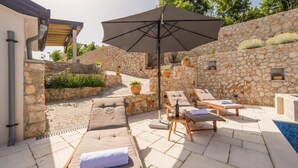 A stone-walled outdoor area with lounge chairs and an umbrella. - Villa Argenta in lovely Aržano, Croatia (Aržano)