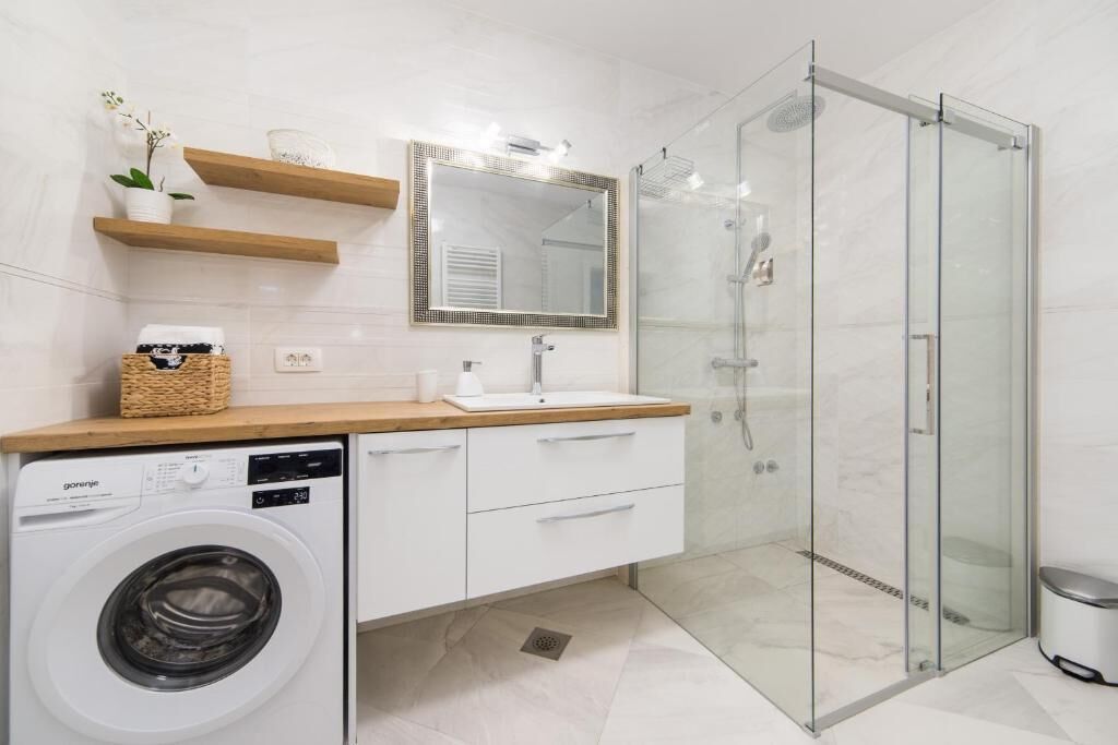 A modern bathroom with a glass shower enclosure, a washing machine, and a wooden countertop with a sink and mirror.