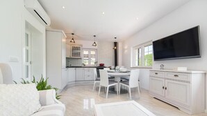 A modern kitchen with white cabinetry, a dining area with white chairs, and a flat-screen TV mounted on the wall. - Villa Argenta in lovely Aržano, Croatia (Aržano)