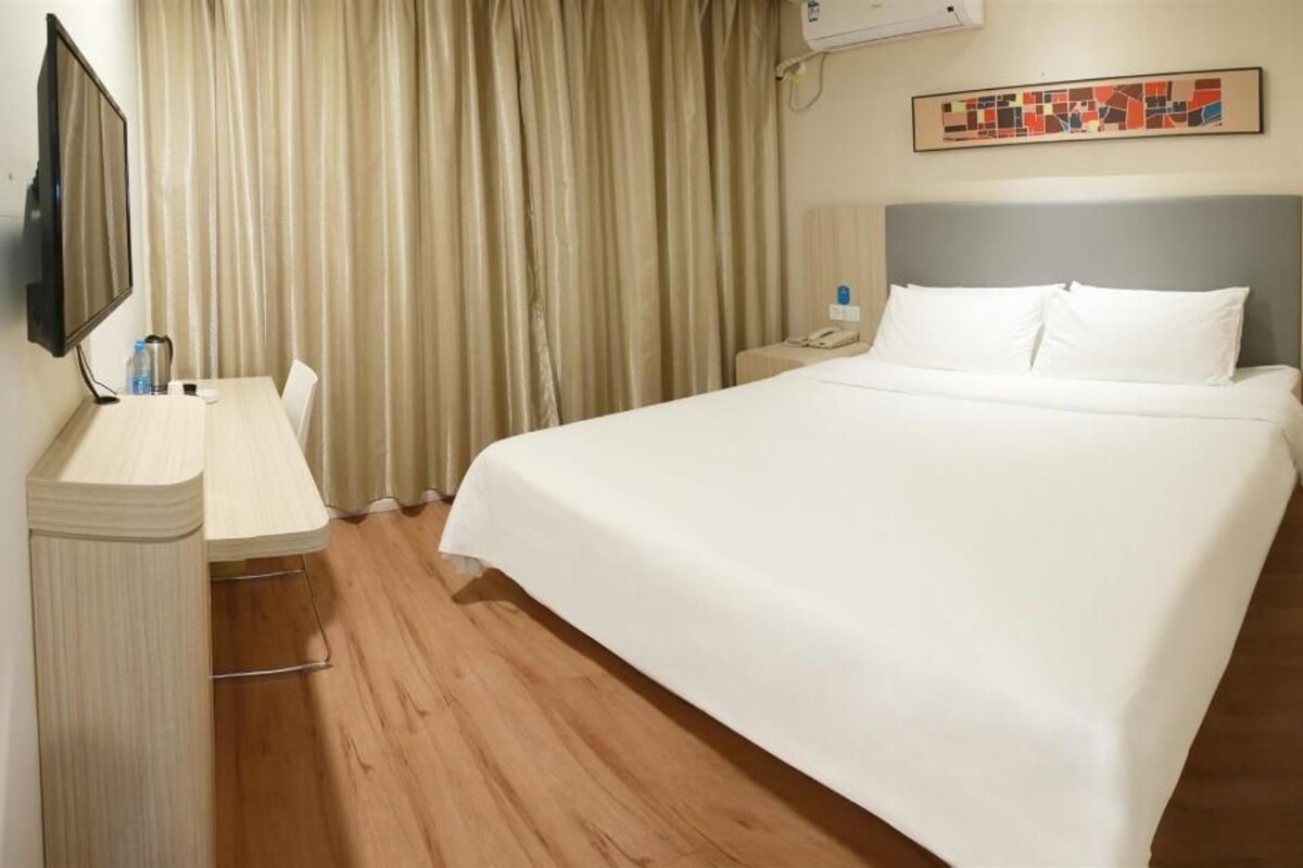 Ein Hotelzimmer mit Bett, Schreibtisch, Stuhl, Fernseher, Telefon und Vorhängen.