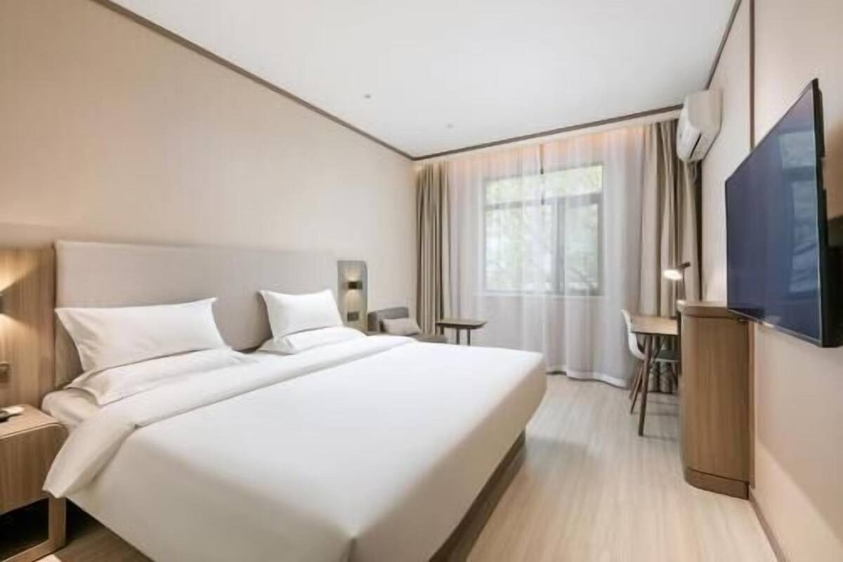 A hotel room with a large bed, a desk, a chair, a TV, and a window with curtains.