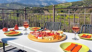 A table set outdoors with a scenic mountain view, a variety of cheeses, meats, and fruits, and two glasses of red wine. - MUSES MOUNTAIN VIEW (Gortyna)