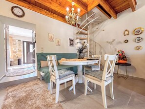 Un espace repas avec une table ronde, des chaises blanches, un lustre et un escalier en colimaçon.