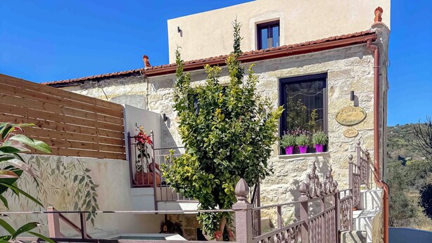 A building with a stone facade, a balcony with potted plants, and a metal gate. - MUSES MOUNTAIN VIEW (Gortyna)