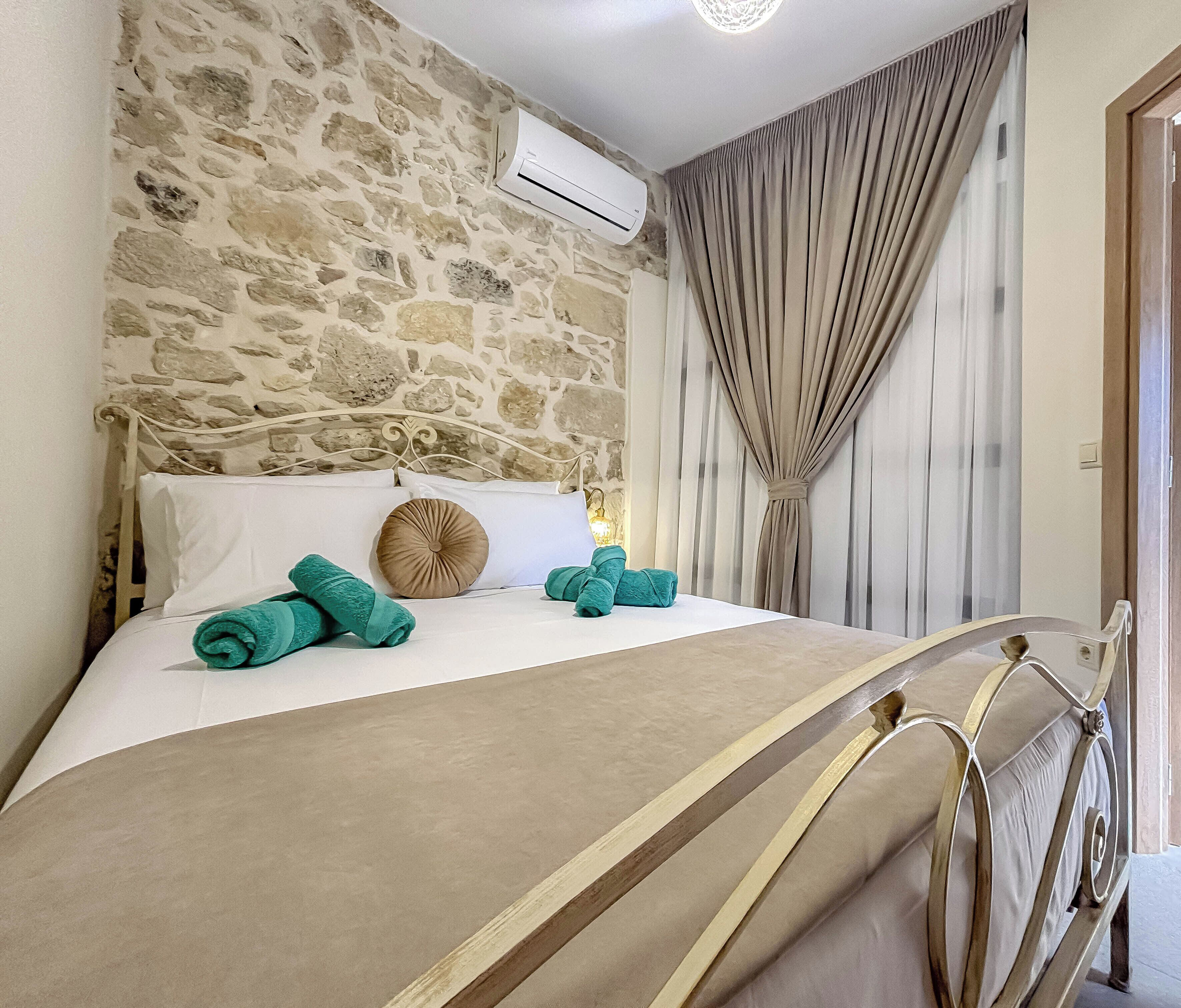 Una cama con toallas enrolladas, un muro de piedra, un equipo de aire acondicionado y una cortina.