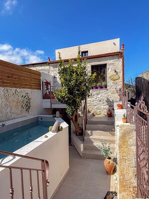 Un bâtiment en pierre doté d’une piscine, d’un escalier menant à un balcon et de plantes en pot.