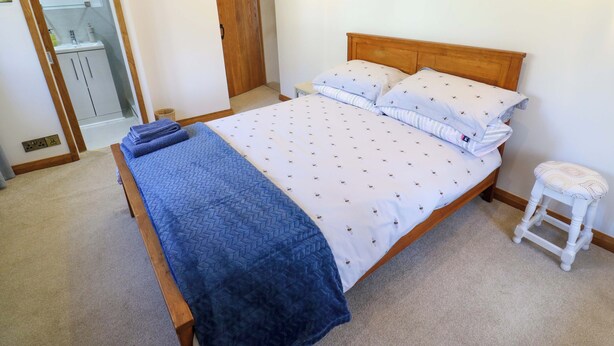 Ein Schlafzimmer mit einem Bett, Nachttischen, einem Holz-Kopfschild, einem kleinen Hocker und einem Kleiderschrank.