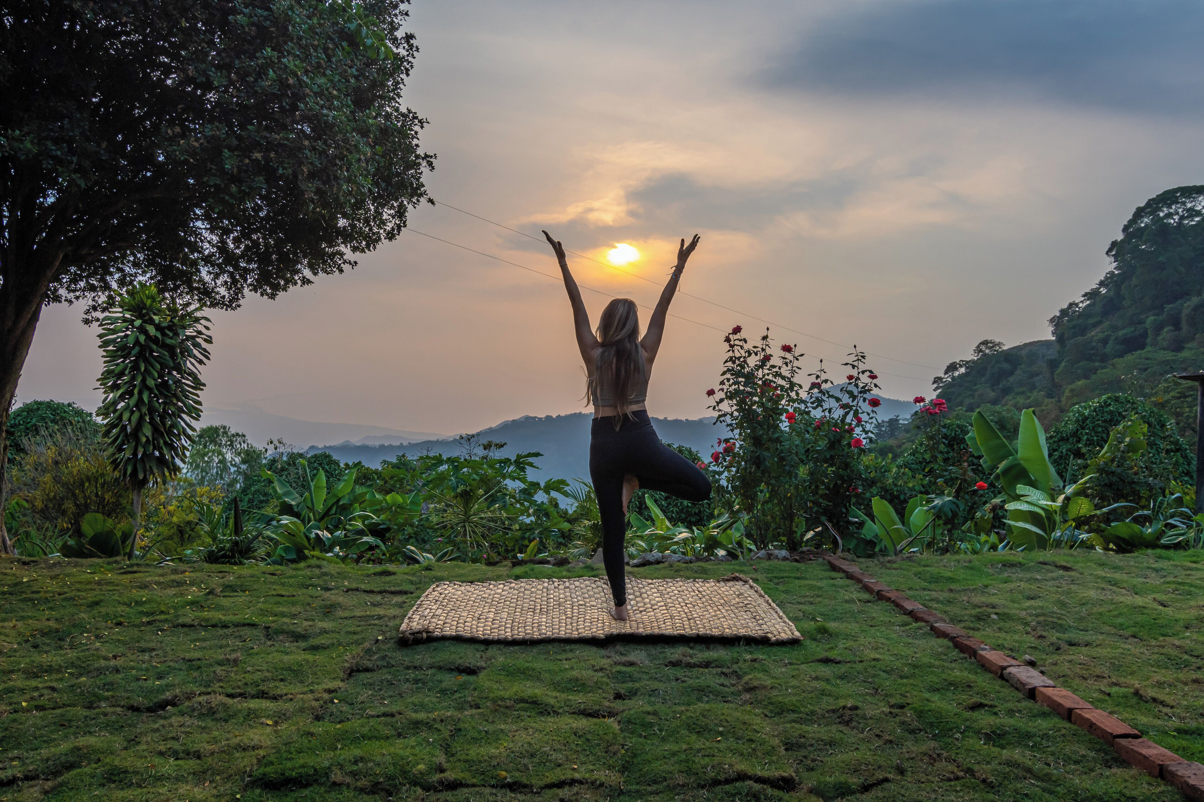 Una persona practicando yoga sobre una esterilla al aire libre, con un paisaje natural de fondo.