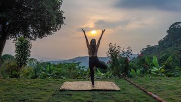 Una persona practicando yoga sobre una esterilla al aire libre, con un paisaje natural de fondo.