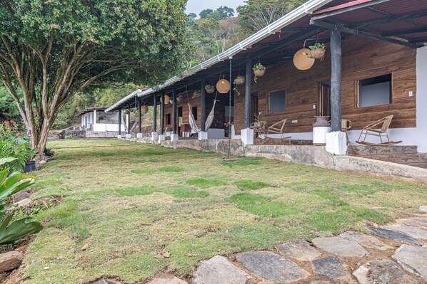 A wooden building with a covered porch, stone pathway, and hanging planters. - Nebula Minca Ecolodge by Xarm Apartments (Santa Marta)