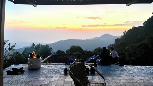 An outdoor seating area with a fire pit, a chair, and a view of the mountains at sunset. - Nebula Minca Ecolodge by Xarm Apartments (Santa Marta)
