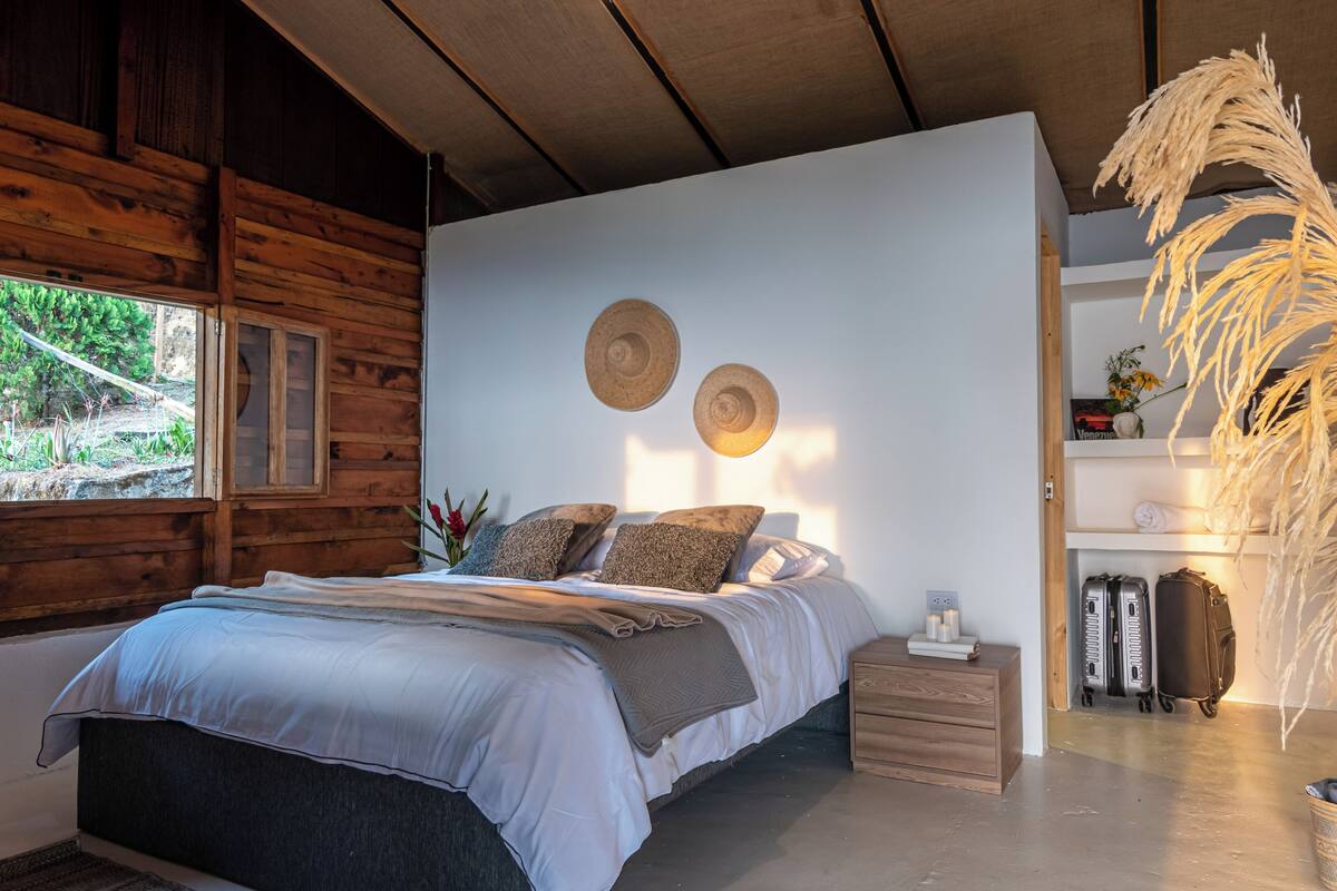 A wooden cabin-style bedroom with a bed, bedside tables, a window, and a shelf with luggage.