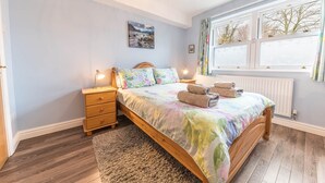 Een slaapkamer met een bed, nachtkastjes, een vloerkleed, een raam met gordijnen en een schilderij aan de muur.