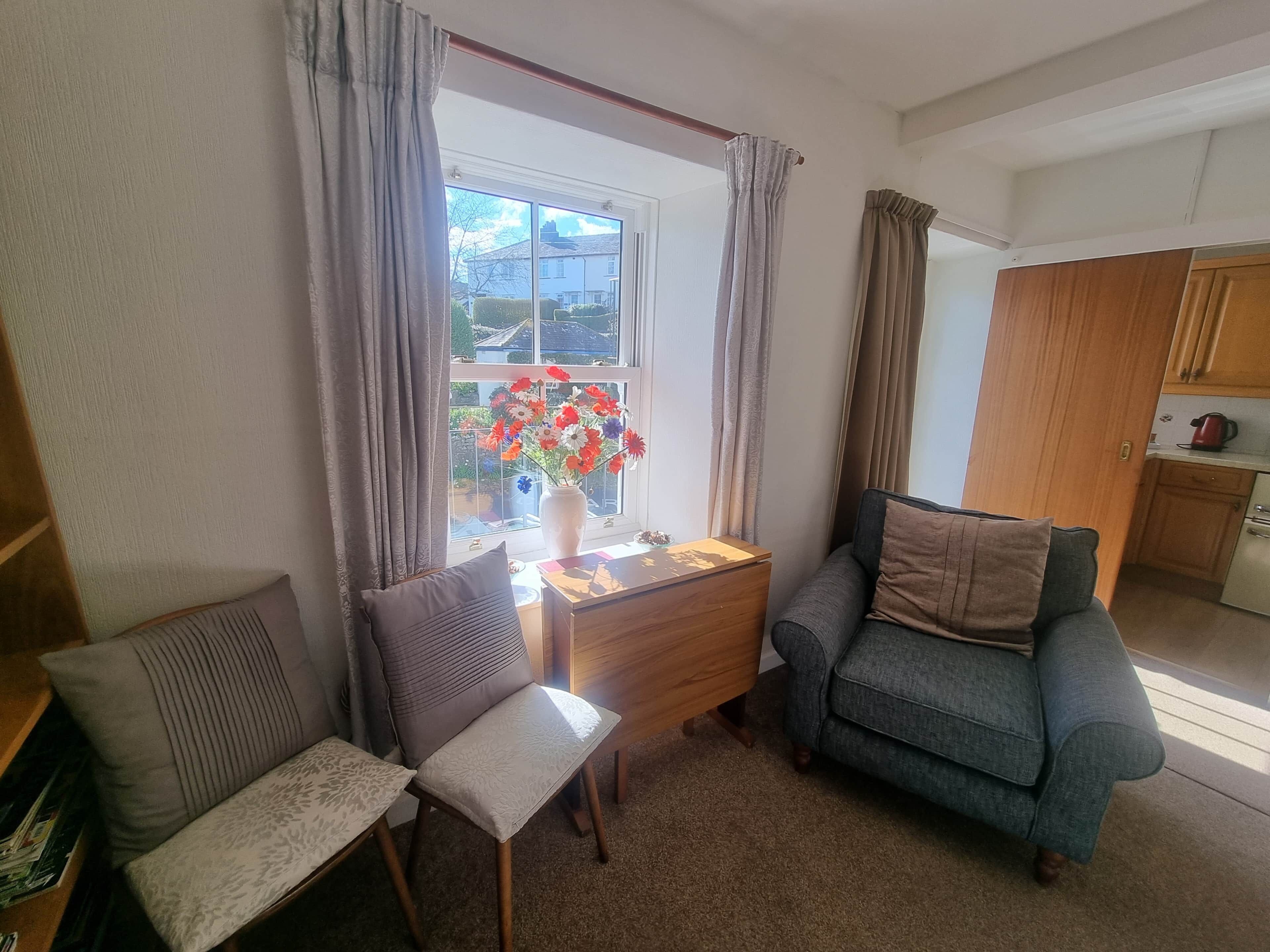 Ein gemütliches Wohnzimmer mit einer Couch, einem Sessel, einem kleinen Tisch und einem Fenster mit Vorhängen.