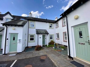 A row of white buildings with green doors and windows, a clear sky, and a paved courtyard. - 8 Howrahs Court, Elliott Park, Keswick (Keswick)