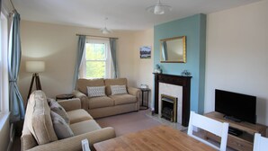 A living room with a sofa, a table, a fireplace, and a television. - Skiddaw, 20 Greta Grove House (Keswick)