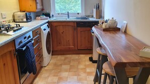 A kitchen with wooden cabinets, a built-in dishwasher, a stove, a washing machine, and a window providing natural light. - Skiddaw, 20 Greta Grove House (Keswick)