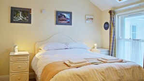 En pænt redt seng med et hvidt sengegavl, et natbord med en lampe og et vindue med gardiner.