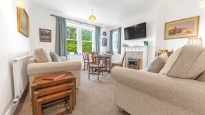 Una sala de estar con chimenea, televisor y comedor con vistas a árboles.