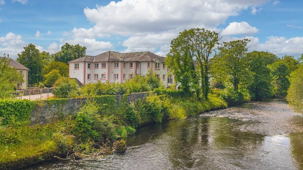 Edificio junto al río con pared de piedra y abundante vegetación.