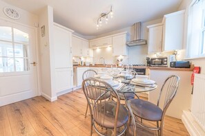 A modern kitchen with white cabinets, a glass dining table, and a stainless steel range hood. - Lilac Cottage, 17 Elm Court, Keswick (Keswick)