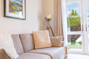 A living room with a sofa, a lamp, a painting, and a view through a glass door. - Lilac Cottage, 17 Elm Court, Keswick (Keswick)