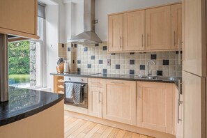 A kitchen with wooden cabinets, a tiled backsplash, a stainless steel sink, and a window overlooking greenery.